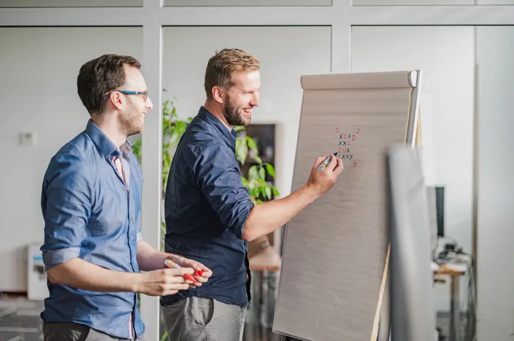 Tomáš Zadák píše fixou na flipchart, vedle stojí kolega a poslouchá